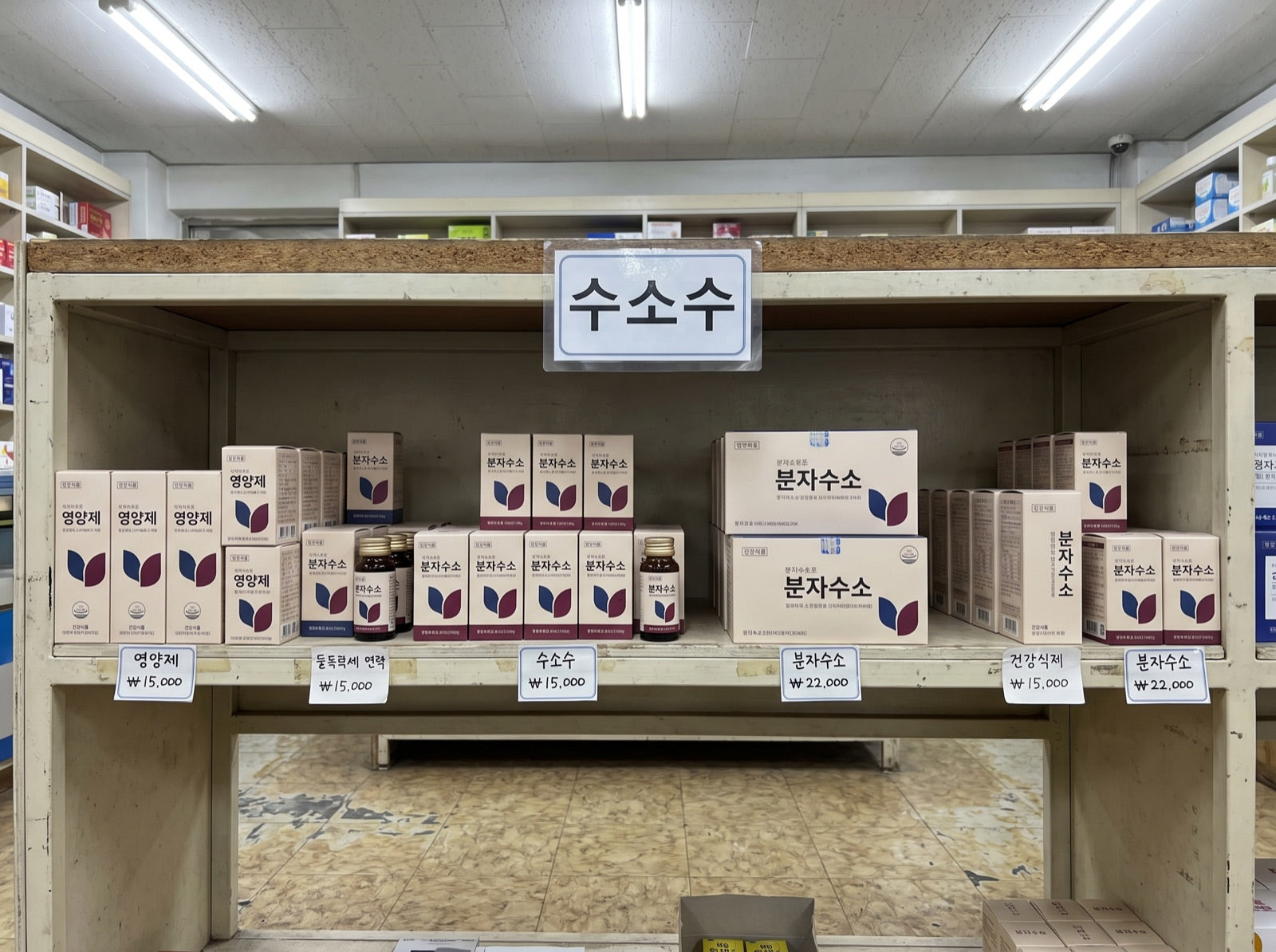 A shelf in an ordinary Korean pharmacy with a sign reading 수소수 and rows of boxes labelled 분자수소, priced in won.