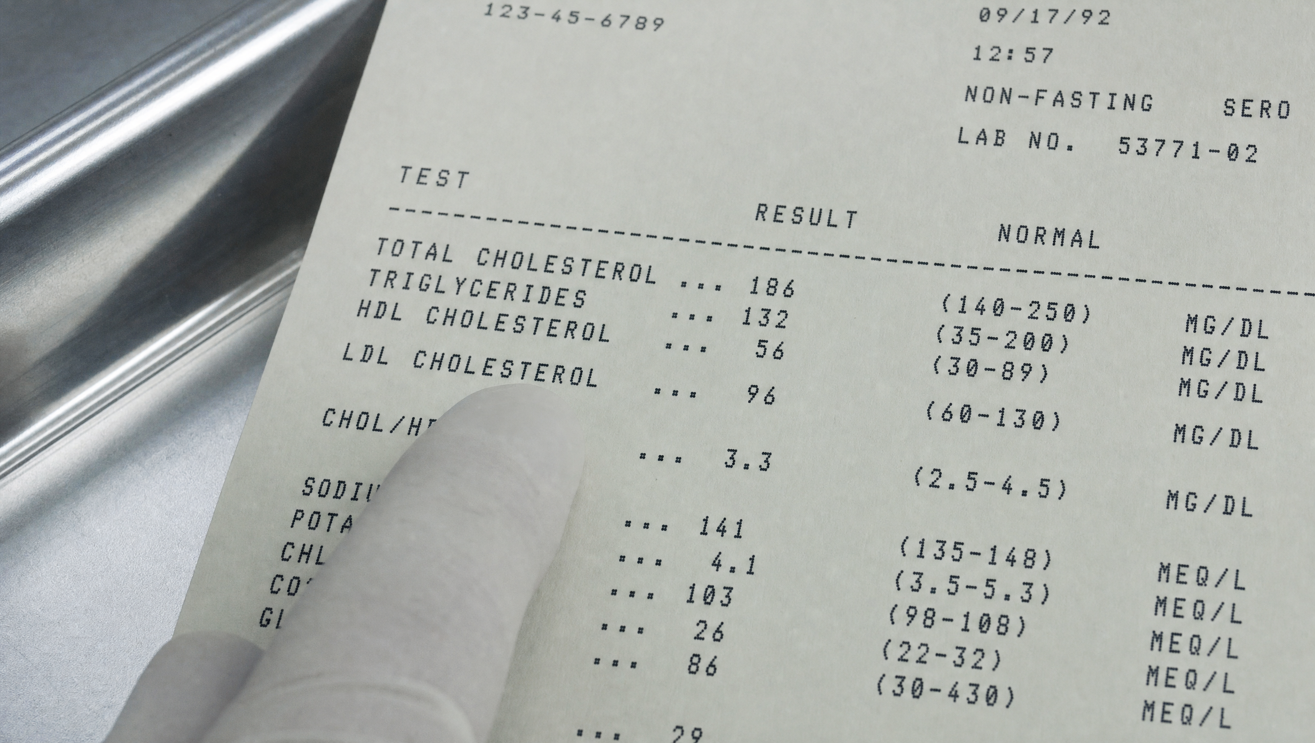 A printed lipid panel held in one hand, a finger resting beside the LDL Cholesterol line, which reads 96 within the normal reference range of 60 to 130.